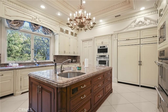 kitchen featuring a sink, dark stone counters, ornamental molding, cream cabinetry, and light tile patterned floors