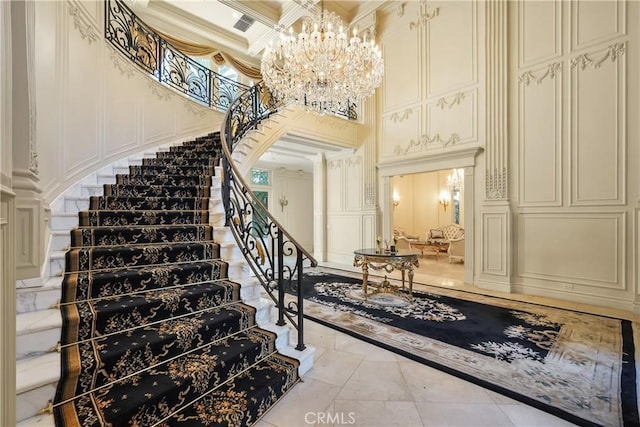 stairway with a towering ceiling, a chandelier, tile patterned flooring, a decorative wall, and ornamental molding