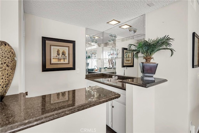 bar featuring dark stone countertops, sink, a textured ceiling, and white cabinets