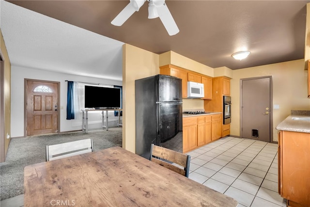 kitchen featuring light tile patterned floors, a textured ceiling, light brown cabinetry, and black appliances