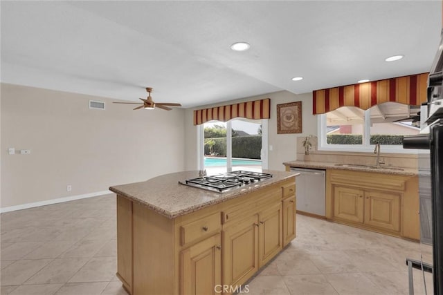 kitchen featuring stainless steel appliances, light stone countertops, sink, and a kitchen island