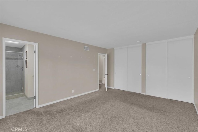 unfurnished bedroom with connected bathroom, light carpet, and two closets