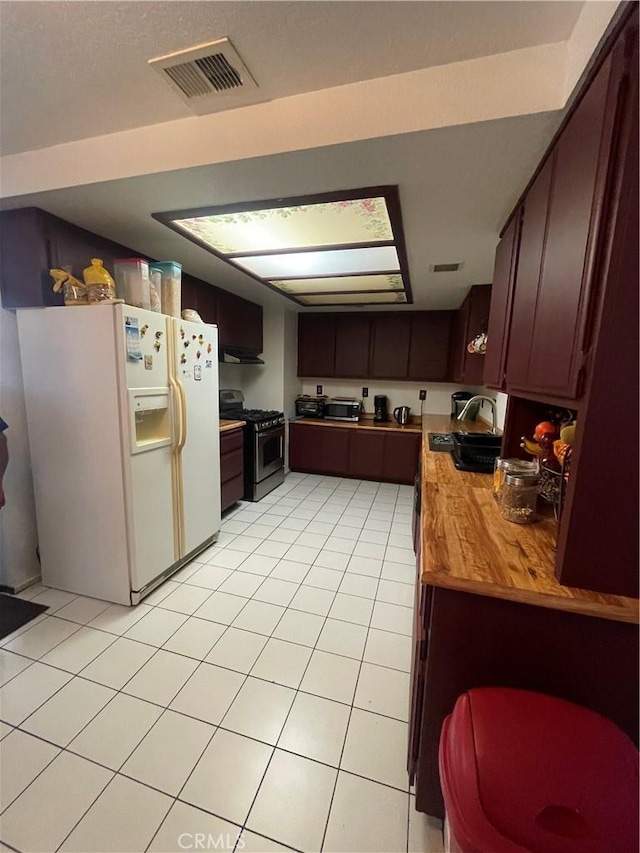 kitchen with butcher block countertops, sink, white fridge with ice dispenser, light tile patterned floors, and gas range