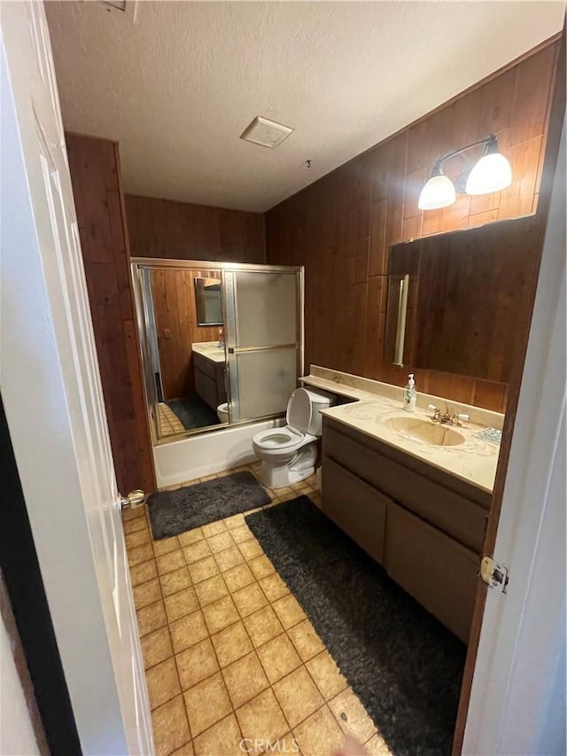 full bathroom with enclosed tub / shower combo, wooden walls, vanity, a textured ceiling, and toilet