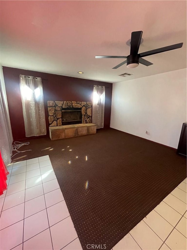 unfurnished living room with tile patterned flooring, a stone fireplace, and ceiling fan