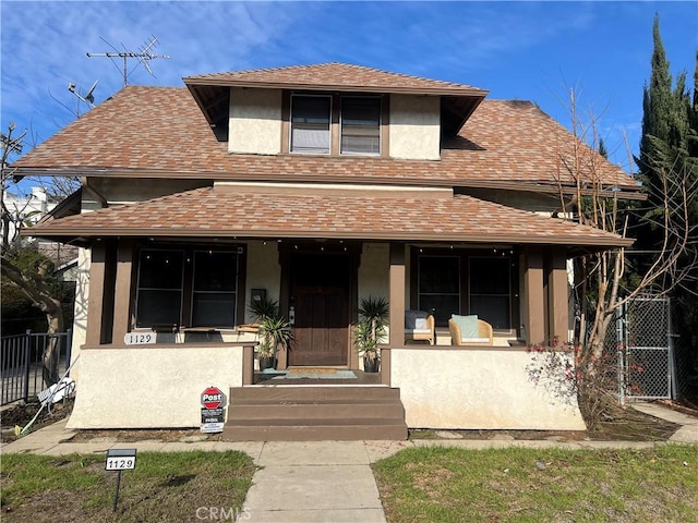 view of front of property with roof with shingles, stucco siding, fence, and covered porch