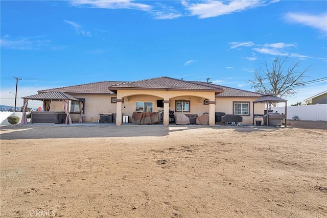 rear view of property featuring a gazebo, a hot tub, and a patio