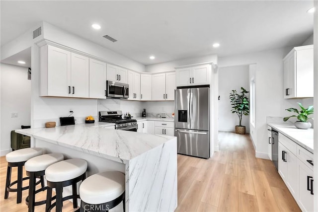 kitchen with appliances with stainless steel finishes, white cabinetry, a kitchen bar, kitchen peninsula, and light stone countertops