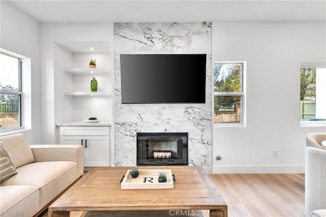 living room featuring built in shelves, a high end fireplace, light hardwood / wood-style flooring, and plenty of natural light