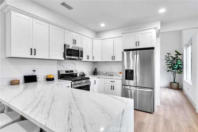 kitchen featuring stainless steel appliances, light stone countertops, white cabinets, and a kitchen breakfast bar