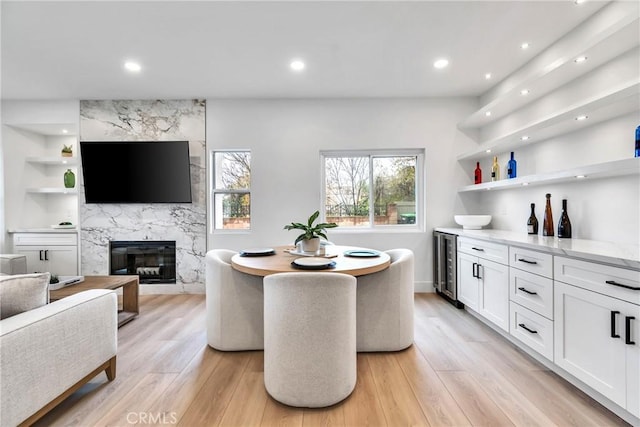 dining space with built in shelves, a high end fireplace, beverage cooler, and light wood-type flooring