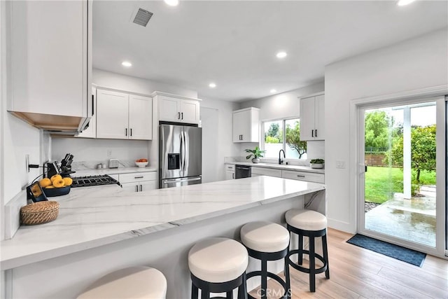 kitchen featuring stainless steel refrigerator with ice dispenser, light stone counters, a kitchen breakfast bar, black dishwasher, and white cabinets