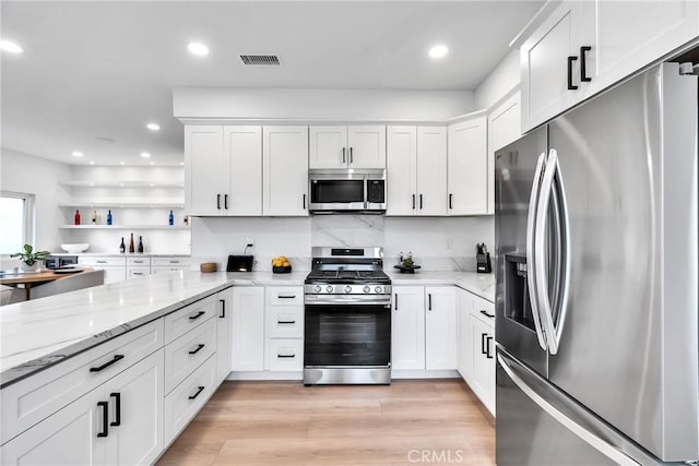 kitchen with stainless steel appliances, light stone countertops, light wood-type flooring, and white cabinets