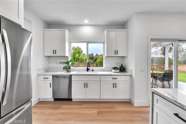 kitchen with white cabinetry, sink, light stone counters, stainless steel appliances, and light wood-type flooring