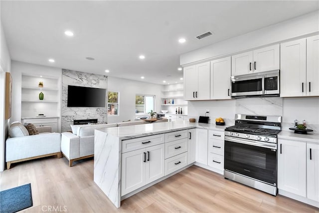 kitchen featuring appliances with stainless steel finishes, white cabinets, light hardwood / wood-style floors, and kitchen peninsula