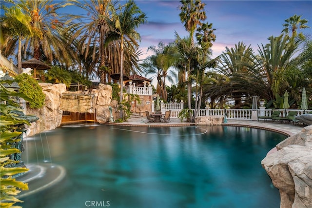 pool at dusk featuring pool water feature and a patio area