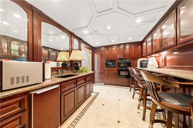 kitchen featuring light tile patterned flooring, double oven, sink, coffered ceiling, and light stone counters