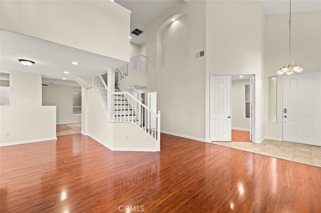 unfurnished living room featuring hardwood / wood-style flooring, a towering ceiling, and a notable chandelier