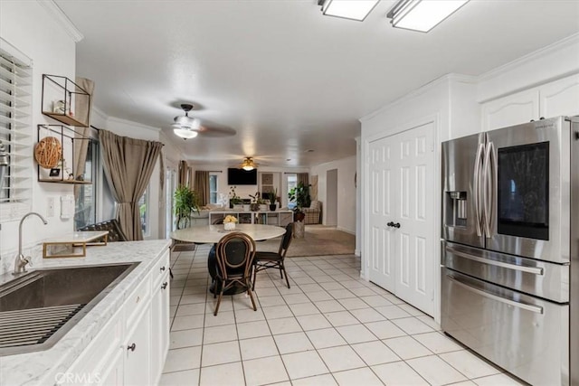 kitchen featuring sink, crown molding, light tile patterned floors, stainless steel fridge, and white cabinets