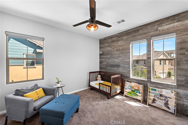 carpeted bedroom with ceiling fan, wood walls, and a nursery area