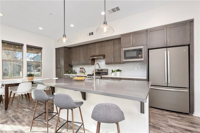 kitchen featuring an island with sink, sink, dark brown cabinets, appliances with stainless steel finishes, and pendant lighting