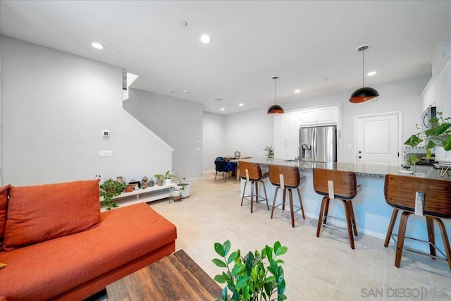 kitchen featuring a kitchen bar, light stone counters, stainless steel fridge, pendant lighting, and white cabinets