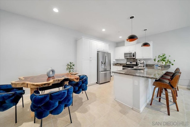 kitchen featuring hanging light fixtures, dark stone countertops, appliances with stainless steel finishes, kitchen peninsula, and white cabinets