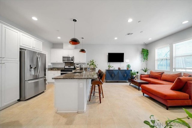 kitchen with appliances with stainless steel finishes, sink, a breakfast bar area, white cabinets, and dark stone counters