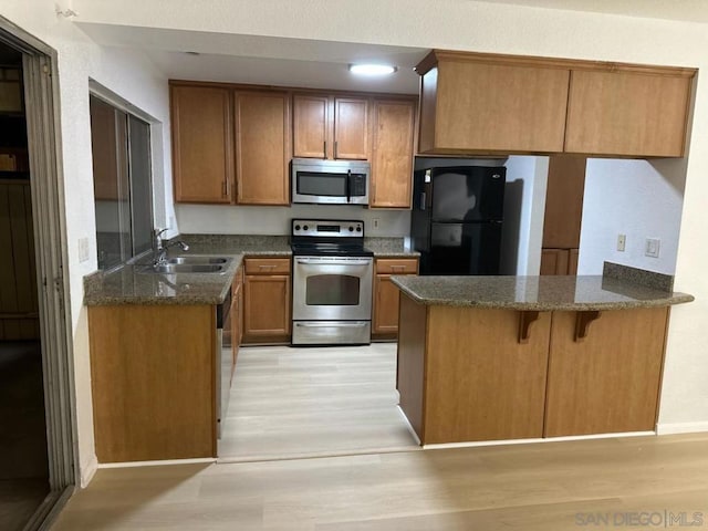 kitchen with appliances with stainless steel finishes, sink, light wood-type flooring, and kitchen peninsula