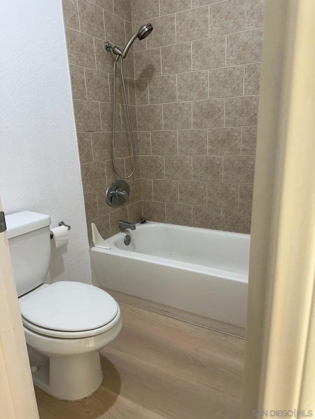 bathroom with tiled shower / bath combo, wood-type flooring, and toilet