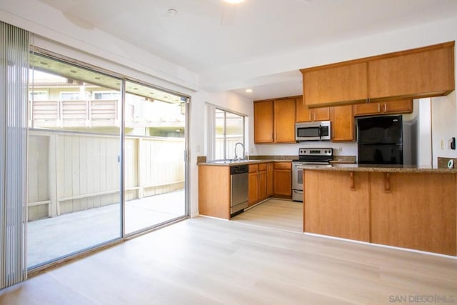 kitchen with sink, a breakfast bar area, appliances with stainless steel finishes, light hardwood / wood-style floors, and kitchen peninsula