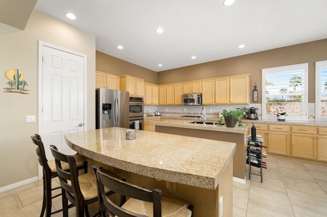 kitchen with light stone countertops, a breakfast bar area, stainless steel appliances, and a center island with sink