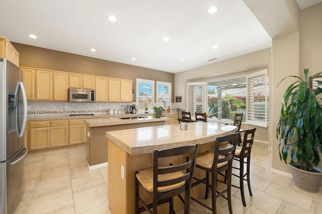 kitchen featuring an island with sink, sink, backsplash, stainless steel appliances, and light brown cabinets