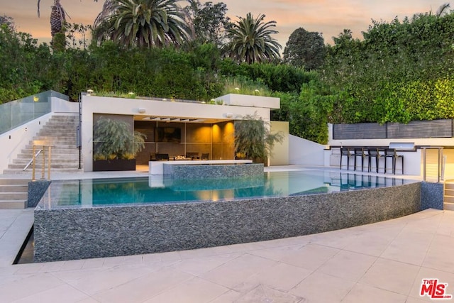 pool at dusk with exterior bar and a patio area