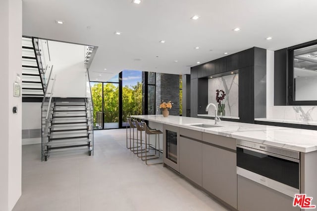 kitchen with a breakfast bar, sink, backsplash, light stone countertops, and a center island with sink