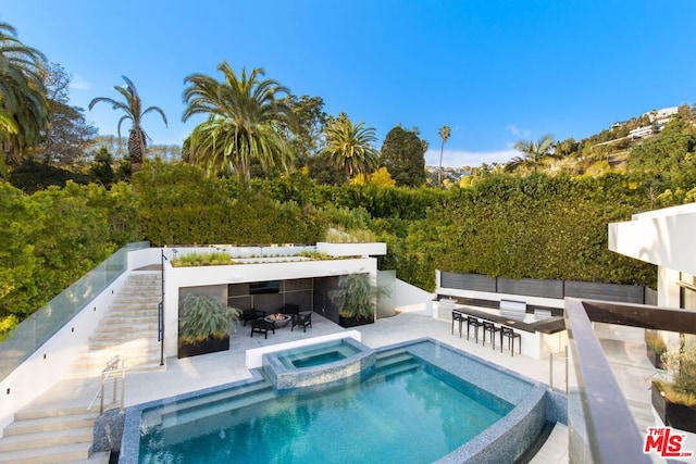 view of swimming pool featuring a bar, an in ground hot tub, and a patio