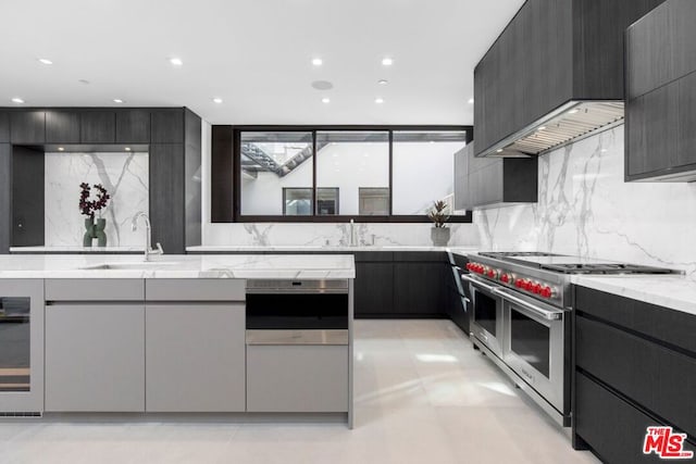 kitchen featuring light stone counters, double oven range, sink, and custom range hood