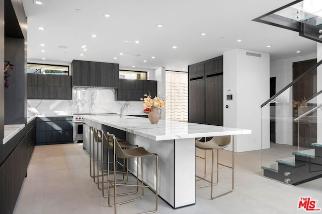 kitchen featuring a breakfast bar area, backsplash, light stone counters, wall chimney range hood, and a spacious island