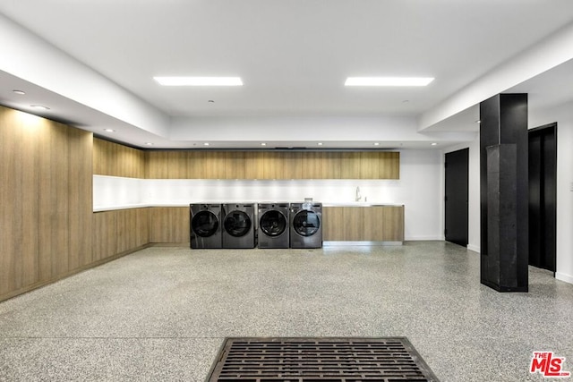 clothes washing area with washer and clothes dryer, sink, wooden walls, and elevator