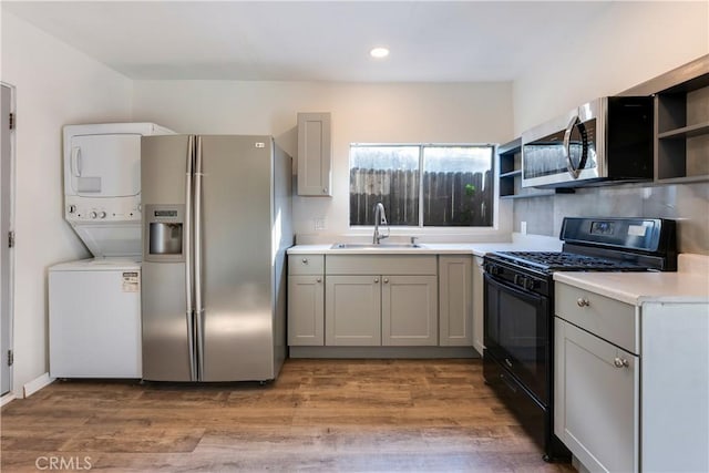 kitchen with stacked washer and clothes dryer, sink, appliances with stainless steel finishes, gray cabinets, and hardwood / wood-style flooring