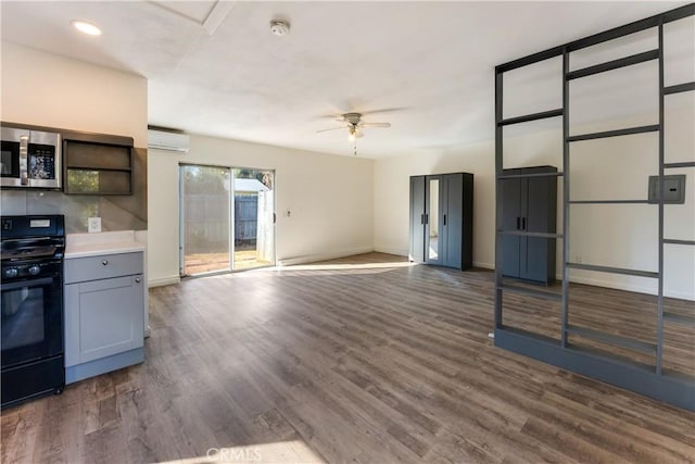 kitchen with dark wood-type flooring, a wall unit AC, black stove, and ceiling fan