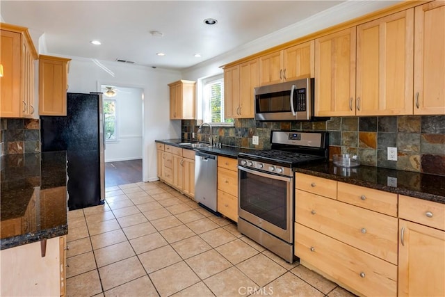 kitchen with sink, light tile patterned floors, appliances with stainless steel finishes, dark stone countertops, and backsplash