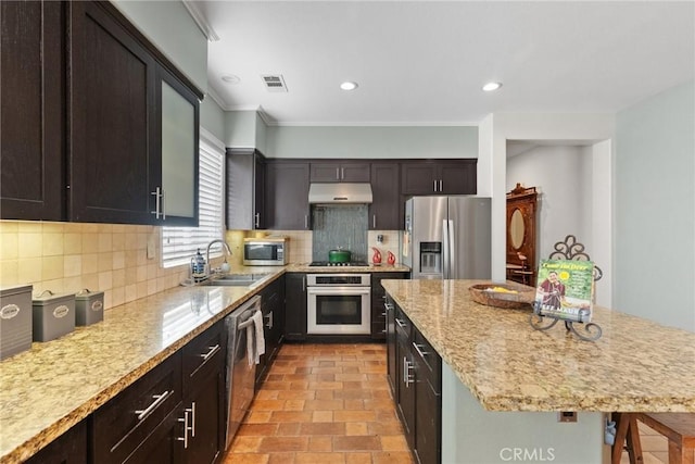 kitchen featuring sink, stainless steel appliances, tasteful backsplash, light stone countertops, and a kitchen bar