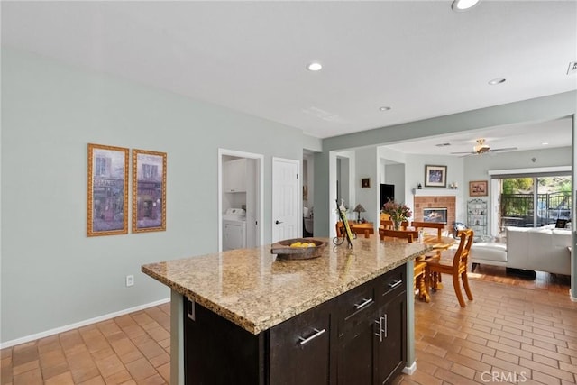 kitchen with light stone counters, a center island, dark brown cabinets, ceiling fan, and washing machine and dryer