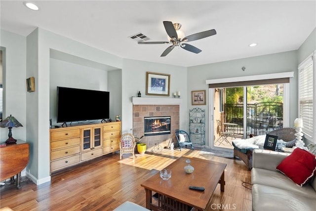 living room with hardwood / wood-style flooring, a tile fireplace, and ceiling fan