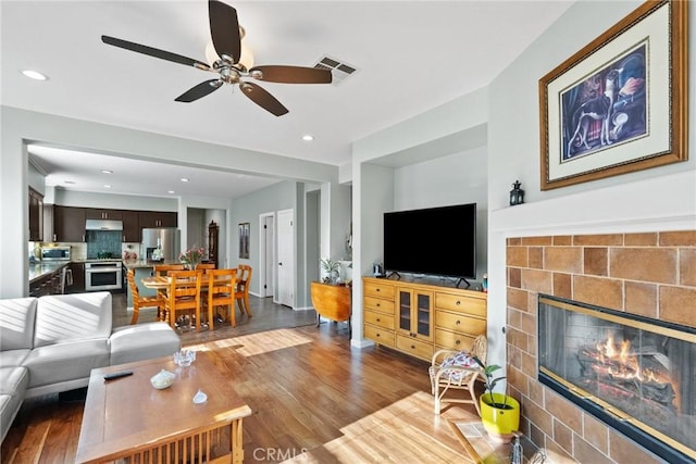 living room featuring a tile fireplace, ceiling fan, and light wood-type flooring