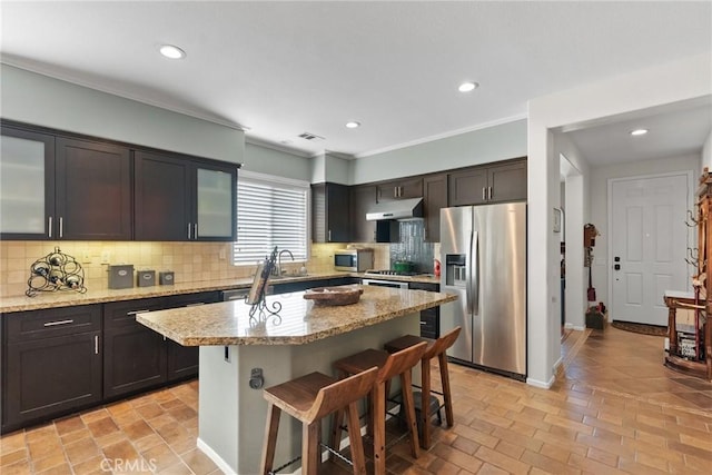 kitchen featuring light stone counters, dark brown cabinetry, appliances with stainless steel finishes, and a center island