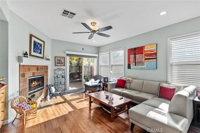 living room with hardwood / wood-style flooring, ceiling fan, and a tiled fireplace