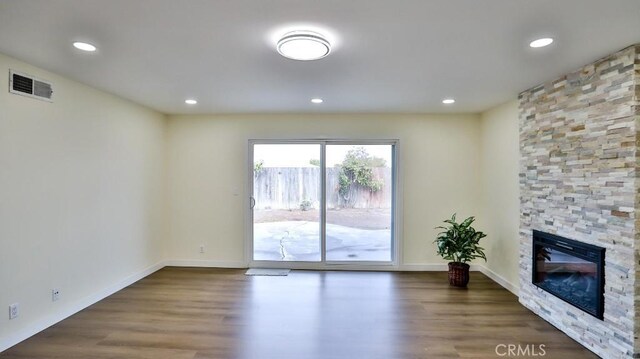 unfurnished living room with wood-type flooring and a stone fireplace