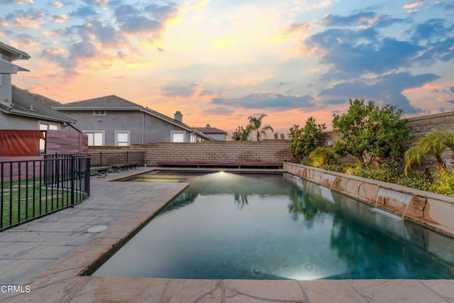 pool at dusk featuring pool water feature and a patio